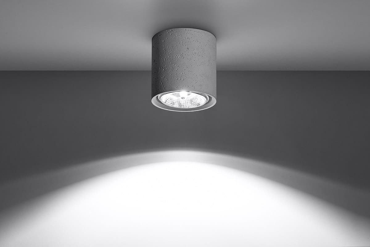 Lampa sufitowa Cullo 1-punktowa w kolorze szarym z betonu, zamontowana na suficie, z okrągłym kloszem odsłaniającym źródło światła. Oświetlenie skierowane w dół tworzy subtelne cienie na ścianie. Prosty, minimalistyczny design.