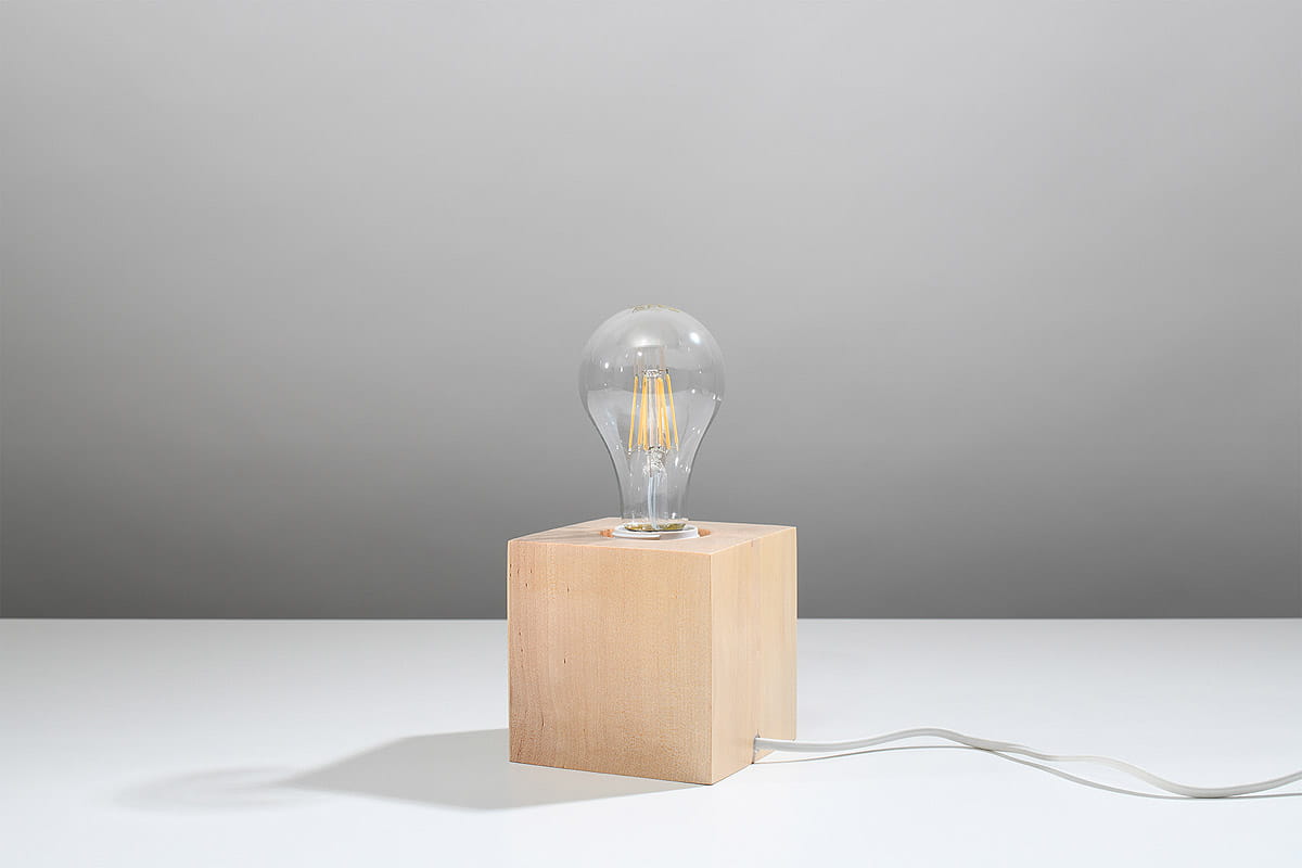 Lampka stołowa Ariz Drewno 1-punktowa SL.0677 z naturalnego drewna w formie sześcianu, z przezroczystą żarówką. Ujęcie frontalne, produkt stoi na białym tle, widoczny kabel zasilający.