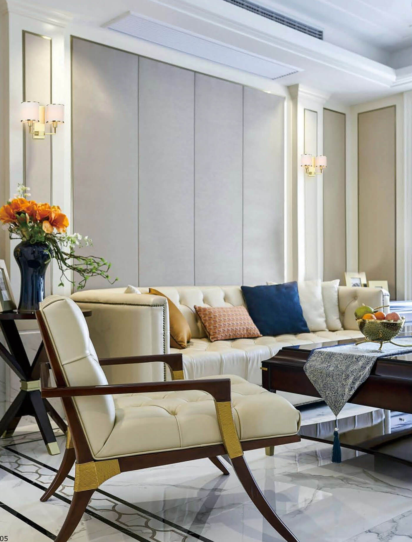 Kinkiet Casa Parette Gold z dwoma punktami świetlnymi, złoty, zamontowany na jasnej ścianie. Obok widoczna elegancka sofa i fotel w jasnym kolorze, w nowoczesnym wnętrzu. W tle elementy dekoracyjne, takie jak kwiaty i poduszki.