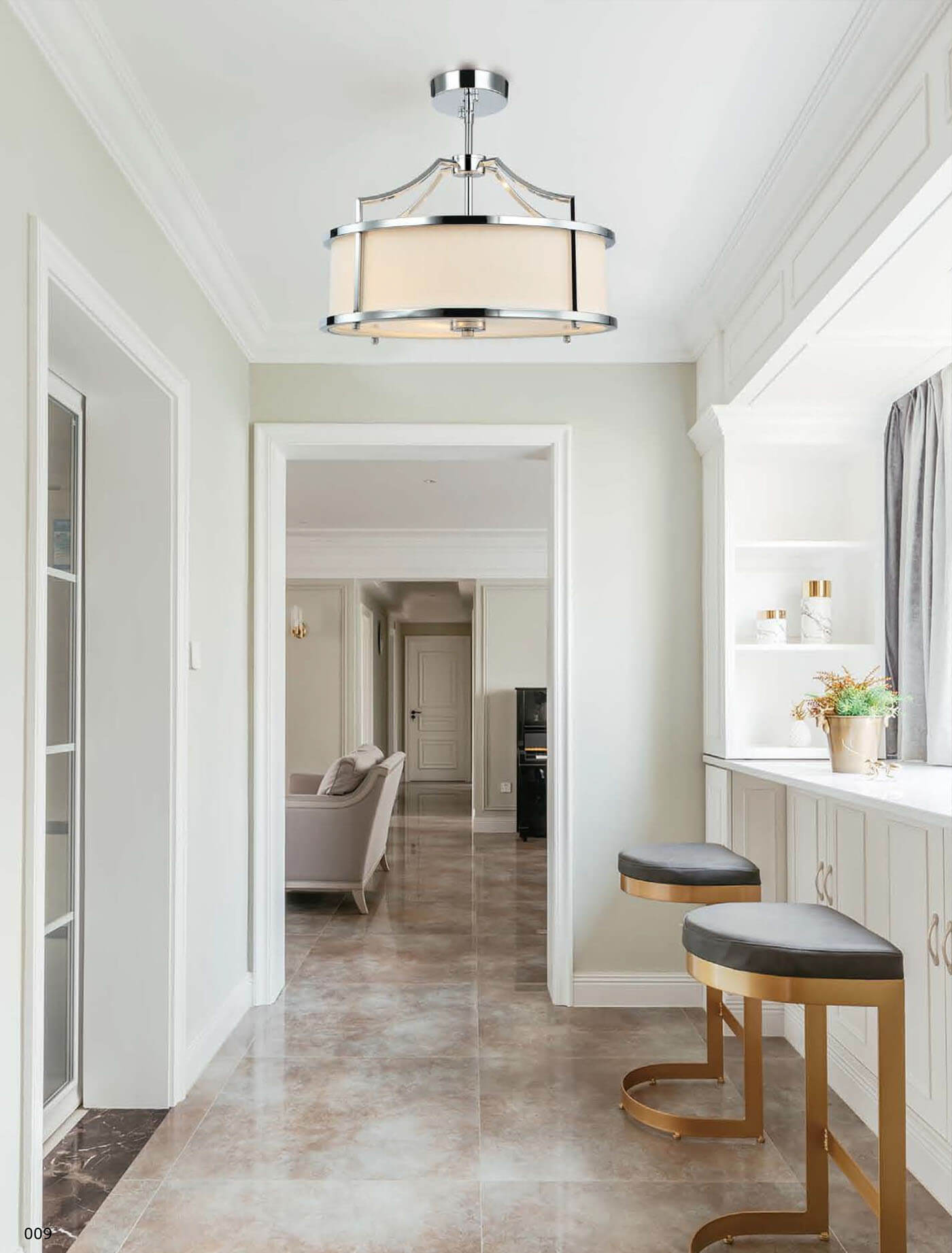 Lampa wisząca Stanza Cromo S w kolorze chromu, z trzema punktami świetlnymi, z okrągłym abażurem w odcieniu kremowym. Zawieszona na metalowym stelażu, z eleganckimi detalami, w nowoczesnym wnętrzu z jasnymi ścianami i podłogą w kolorze beżowym.