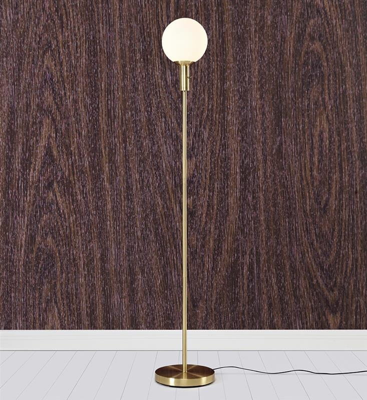 Lampa podłogowa Minna w kolorze mosiądzu z okrągłą, białą kloszem. Stojąca, z cienką nogą i okrągłą podstawą. Ujęcie frontalne na tle ciemnego drewna. Kabel zasilający widoczny u podstawy.