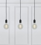 Lampa wisząca Sky 3-punktowa w kolorze czarnym z trzema szklanymi żarówkami. Kable wisi na równych długościach, a całość zamocowana na jasnym tle z dekoracyjnymi panelami. Prosty, nowoczesny design.