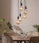 Lampa wisząca Sky z pięcioma punktami świetlnymi, czarna, z przezroczystymi żarówkami w okrągłych kloszach. Zawieszona na długich, czarnych przewodach, w aranżacji z drewnianym stołem i roślinami w tle na jasnej ścianie.