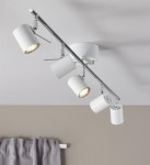 Hyssna lampa sufitowa (spot) 5-punktowa w białym kolorze, zamontowana na metalowej listwie. Posiada pięć regulowanych reflektorów, z których jeden jest widoczny z włączonym światłem. Tło w odcieniach beżu z zasłoną w szarości.