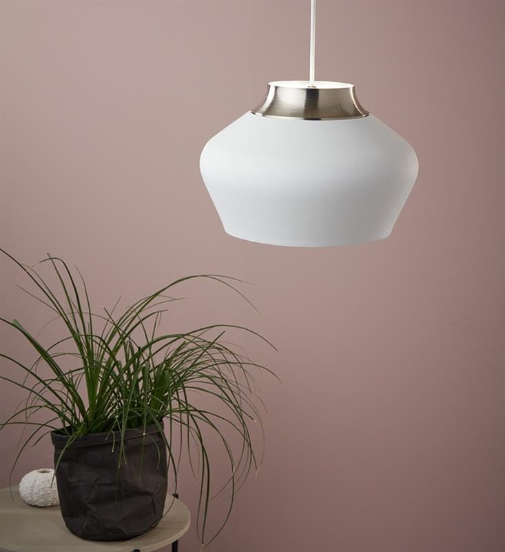 Lampa wisząca Kom D31 w kolorze białym z metalowym, stalowym detalem na górze. Posiada zaokrąglony kształt, zawieszona na cienkim kablu. W tle widoczna doniczka z rośliną na stoliczku, na jednolitym różowym tle.