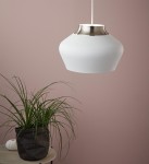 Lampa wisząca Kom D31 w kolorze białym z metalowym, stalowym detalem na górze. Posiada zaokrąglony kształt, zawieszona na cienkim kablu. W tle widoczna doniczka z rośliną na stoliczku, na jednolitym różowym tle.