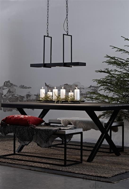 Czarna lampa wisząca Tray LED 3-punktowa, zawieszona na łańcuchach, umieszczona nad drewnianym stołem. W tle widoczna ściana z odrapanym tynkiem oraz dekoracje, takie jak świeczniki z białymi świecami i zielona choinka.
