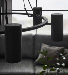 Czarna lampa wisząca Porto z sześcioma punktami świetlnymi, o cylindrycznym kształcie i matowej fakturze. Ujęcie zbliżeniowe, pokazujące detale mocowania i okrągłą konstrukcję, zawieszona nad szarym sofą w tle.