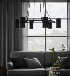 Czarna lampa wisząca Porto z 6 punktami świetlnymi, zawieszona nad szaro-skalowym sofą. W tle duże okno z zasłonami oraz roślinność w ozdobnym doniczku. Kształt cylindryczny lampy, minimalistyczny design.