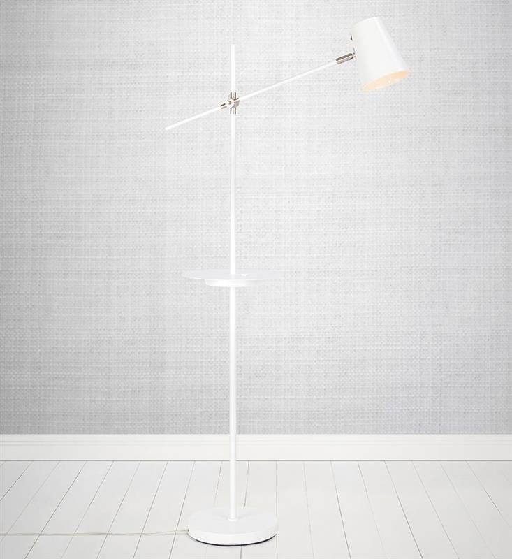 Biała lampa podłogowa Hudson z jednym punktem świetlnym, wyposażona w stół do odkładania. Posiada metalową podstawę, regulowany klosz oraz złącze USB. Ustawiona w pionie na jasnej podłodze, z tłem w odcieniu szarości.