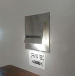 Oprawa schodowa Fero LED 230V w neutralnej barwie 4000K, wykonana ze stali nierdzewnej, montowana na ścianie. Posiada prostokątny kształt z wcięciem, emitującym światło w dół. Widoczne oznaczenie OPRAWA FERO 4000K na metalowej tabliczce.