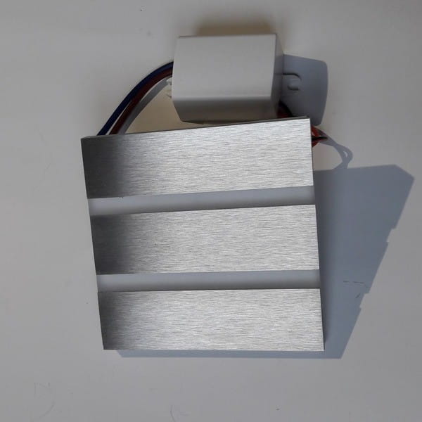 Oprawa schodowa Vox LED 230V w neutralnej barwie 4000K, z aluminiowym wykończeniem. Ułożona frontalnie, z widocznym złączem elektrycznym oraz trzema poziomymi szczelinami, które umożliwiają emitowanie światła.