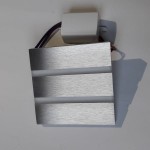 Oprawa schodowa Vox LED 230V w neutralnej barwie 4000K, z aluminiowym wykończeniem. Ułożona frontalnie, z widocznym złączem elektrycznym oraz trzema poziomymi szczelinami, które umożliwiają emitowanie światła.