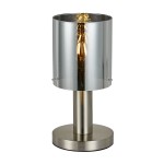 Lampka stołowa Sardo 1-punktowa z niklu satynowego, z cylindrycznym kloszem w metalicznym wykończeniu. Posiada okrągłą podstawę i widoczną żarówkę w środku. Ujęcie frontalne, produkt stoi na płaskiej powierzchni.