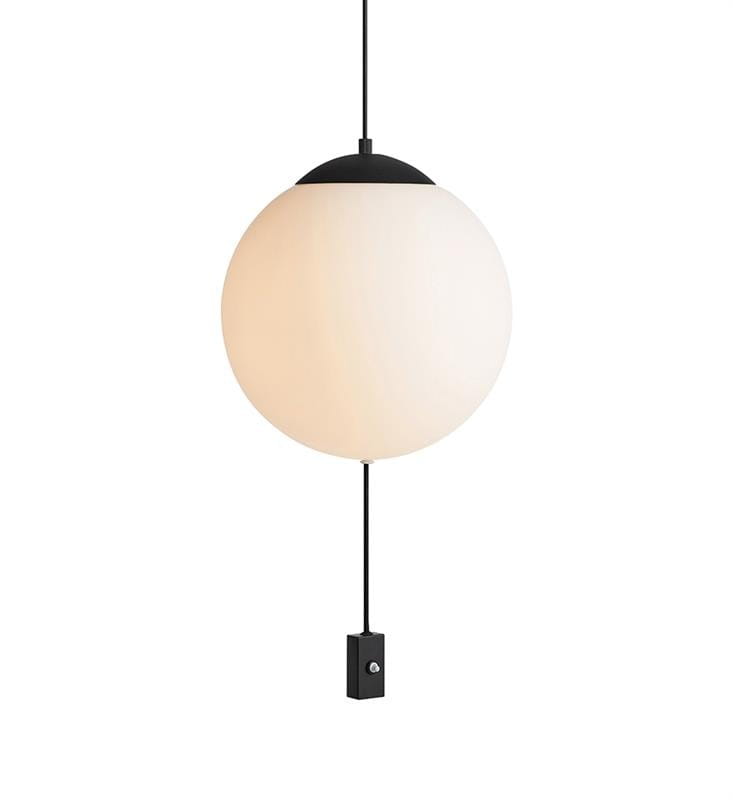 Lampa wisząca 3-punktowa Here, okrągła kula z mlecznego szkła, zawieszona na czarnym przewodzie. U podstawy widoczny prostokątny element z metalowym przyciskiem. Całość w minimalistycznym stylu.