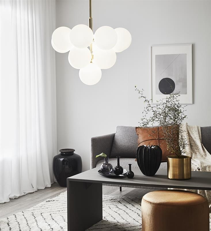 Merlot lampa wisząca 13-punktowa w złotym i białym kolorze, z okrągłymi, mlecznymi kloszami, zawieszona nad stolikiem w nowoczesnym wnętrzu. Lampa ma prosty, elegancki design, idealna do salonu. W tle widoczna kanapa i dekoracje.