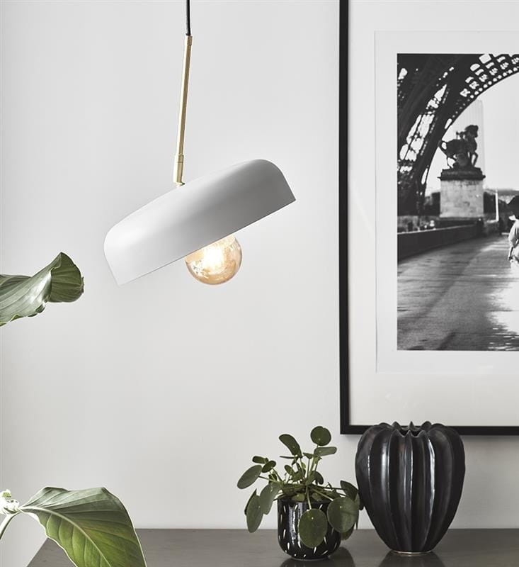 Lampa wisząca Caen 1-punktowa w kolorze szarym z elementami złota szczotkowanego. Okrągły klosz z metalowym wykończeniem, zawieszony na czarnym przewodzie. W tle rośliny doniczkowe oraz czarna dekoracja.