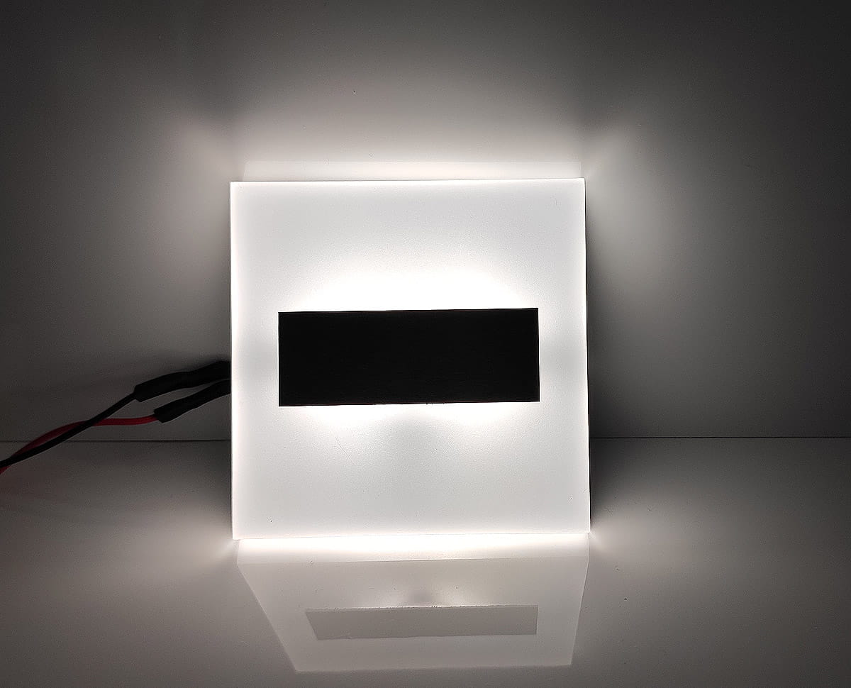 Lumi LED oprawa schodowa 230V, prostokątna, o zimnej barwie 6500K. Biała, matowa powierzchnia z czarnym elementem centralnym. Ujęcie frontalne, z przewodami elektrycznymi widocznymi z boku. Idealna do oświetlenia schodów.