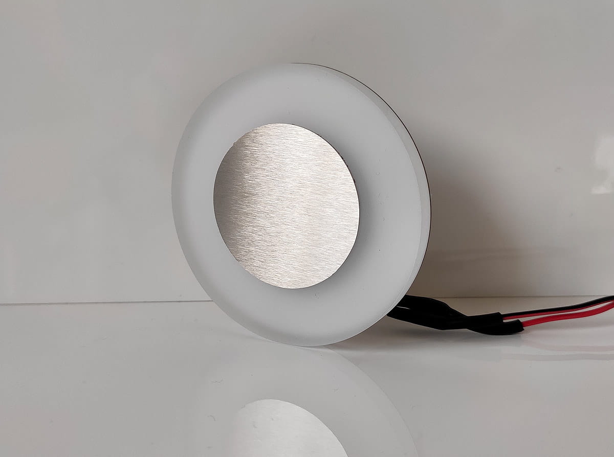 Oti LED oprawa schodowa 230V w neutralnej barwie 4000K, okrągła, z białym plastikiem i metalową, szczotkowaną powierzchnią. Z przewodami elektrycznymi, ustawiona w pozycji leżącej, na jednolitym tle. Idealna do oświetlenia schodów.