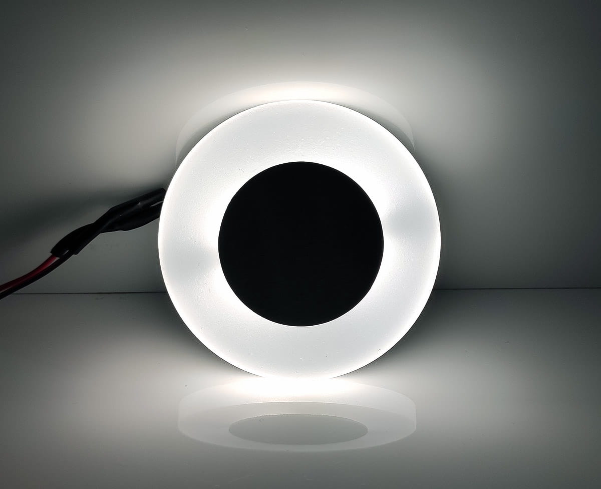 Oprawa schodowa Oti LED 230V z barwą zimną 6500K, okrągła, z matowym białym kloszem i czarnym wnętrzem. Widoczny kabel zasilający. Produkt leży na gładkiej powierzchni, oświetlony równomiernie, co podkreśla jego kształt.