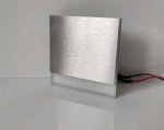 Oprawa schodowa Berg LED 230V w ciepłej barwie 3000K, z metalową szczotkowaną obudową oraz białym, matowym elementem emitującym światło. Ujęcie z boku, ukazujące kable zasilające. Idealna do oświetlenia schodów lub korytarzy.