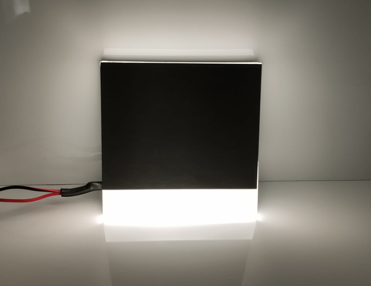 Oprawa schodowa Berg LED 230V w kształcie kwadratu, w kolorze czarnym z białym podświetleniem na dolnej krawędzi. Widoczne przewody elektryczne. Barwa światła neutralna 4000K, montowana na ścianie lub w podłodze.