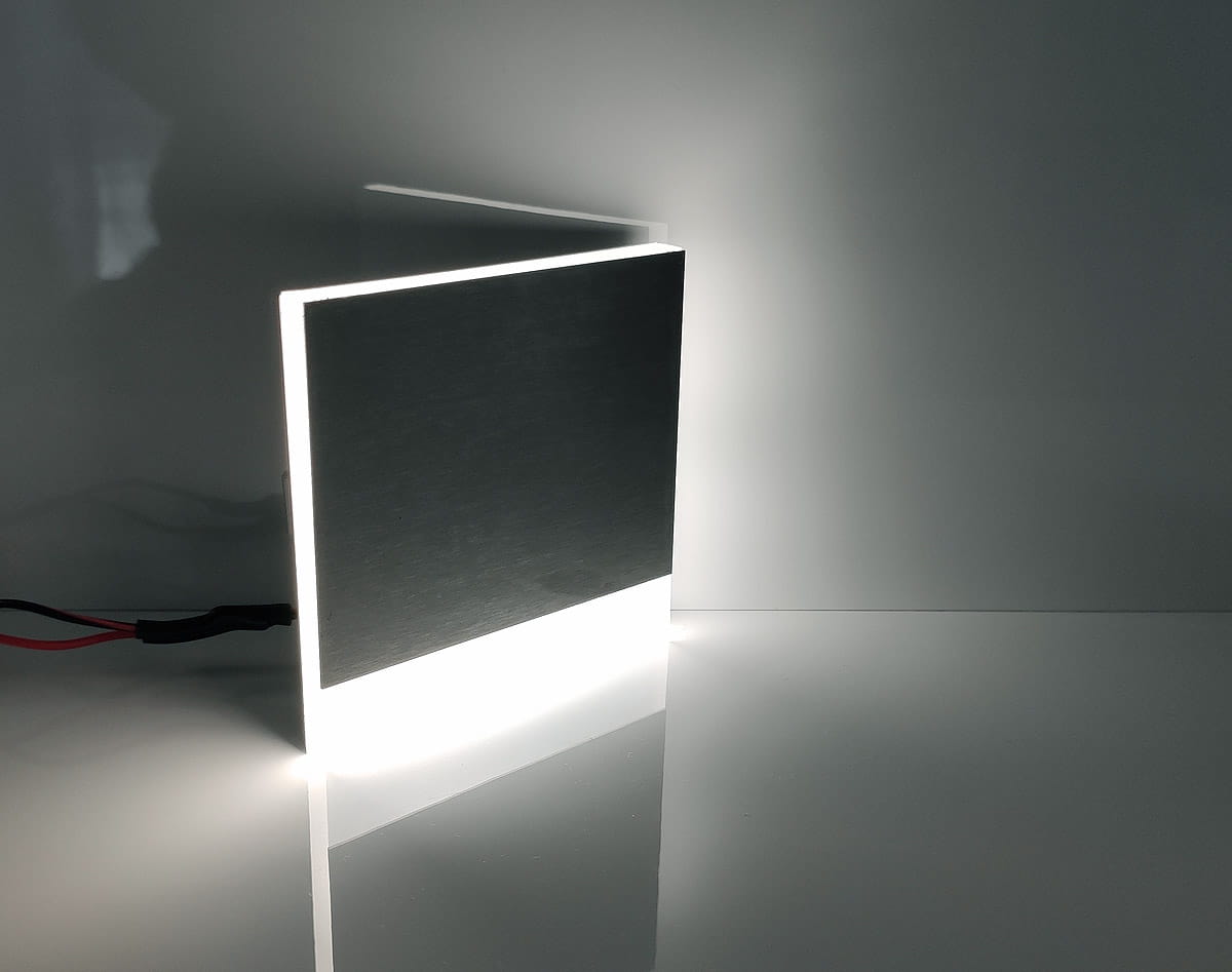 Berg LED oprawa schodowa 230V, z zimnym światłem 6500K. Produkt w kształcie prostokąta, metaliczna powierzchnia z błyszczącym wykończeniem, podświetlona od spodu. Ujęcie z boku, ukazujące krawędź oraz przewody zasilające.