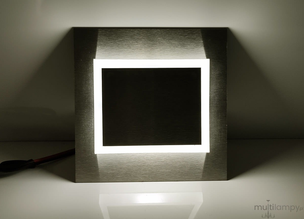 Oprawa schodowa Deco LED 230V o neutralnej barwie 4000K, z prostokątnym, metalicznym wykończeniem. Zainstalowana w poziomie, z diodowym podświetleniem w kształcie ramki, na jasnym tle. Widoczne kable zasilające.