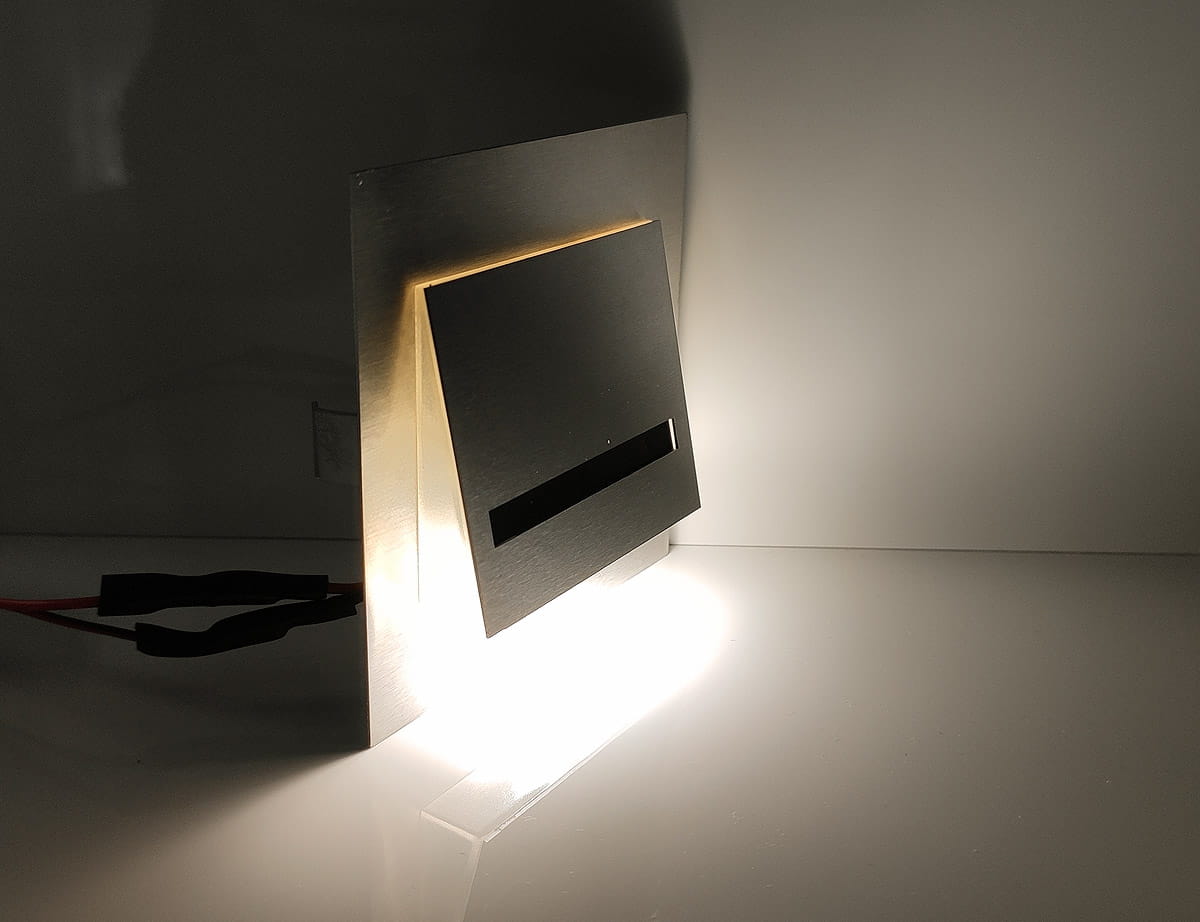 Fero LED oprawa schodowa 230V w neutralnej barwie 4000K, z metalową obudową i szczeliną emitującą światło. Ujęcie z boku, oprawa ustawiona na płaskiej powierzchni, z widocznym przewodem zasilającym. Tło jasne, minimalistyczne.