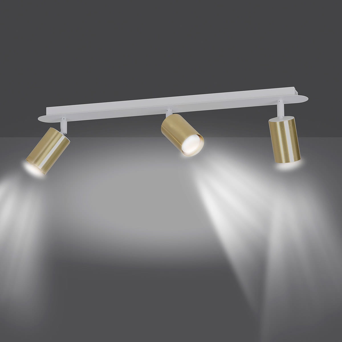 Biała lampa sufitowa Zen z trzema punktami świetlnymi w złotych oprawach, montowana na prostokątnej listwie. Ujęcie z przodu, ukazujące rozproszone światło na tle szarym.