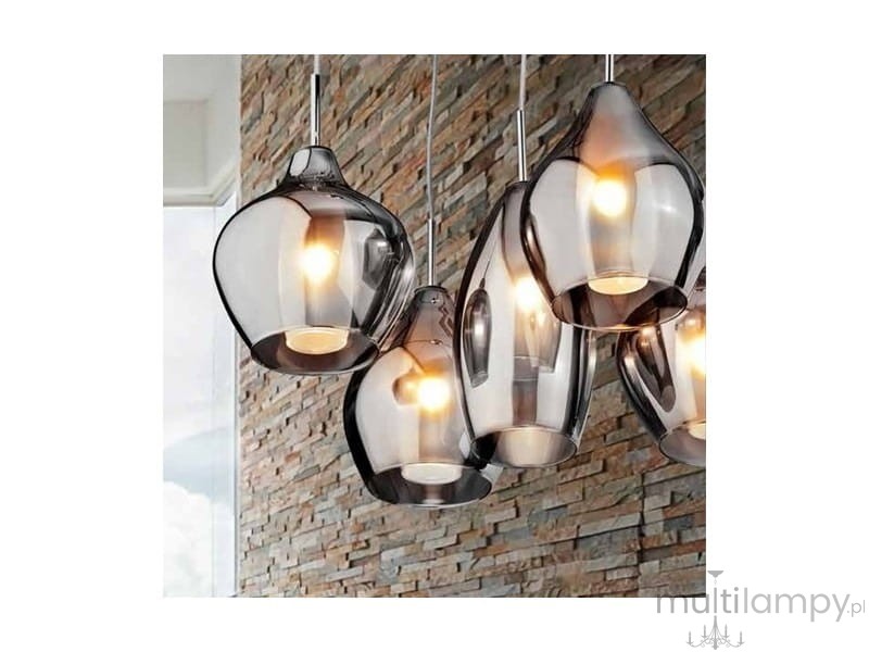 Lampa wisząca Amber Milano 5-punktowa w chromowanej obudowie z transparentnymi kloszami. Klosze mają różne kształty, emitując ciepłe światło. Produkt zawieszony na cienkich linkach, na tle kamiennej ściany.