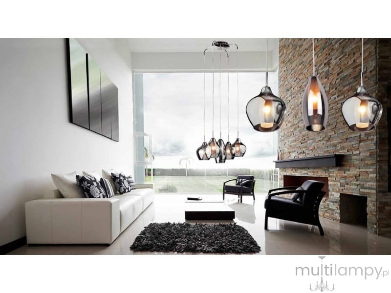 Lampa wisząca Amber Milano 5-punktowa w chromie, z różnymi kloszami w kształcie kropli, zawieszona w nowoczesnym wnętrzu z białą sofą, czarnym dywanem i kominkiem. Klosze o szklanej fakturze, emitujące ciepłe światło.