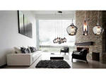 Lampa wisząca Amber Milano 5-punktowa w chromie, z różnymi kloszami w kształcie kropli, zawieszona w nowoczesnym wnętrzu z białą sofą, czarnym dywanem i kominkiem. Klosze o szklanej fakturze, emitujące ciepłe światło.