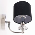 Kinkiet Abu Dhabi 1-punktowy w kolorze chromu i czerni. Posiada cylindryczny klosz z czarnej tkaniny oraz metalową, błyszczącą podstawę. Ujęcie z boku, montowany na ścianie. Widoczny przycisk włącznika.