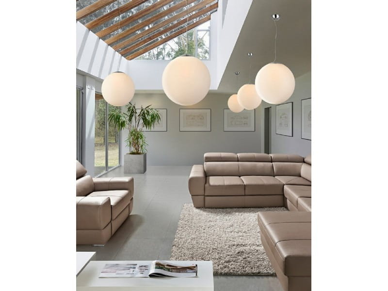 Lampa wisząca White Ball 40, 1-punktowa, z białym, okrągłym kloszem, zawieszona w jasnym wnętrzu z dużymi oknami i roślinnością. W tle widoczna skórzana sofa oraz stół na dywanie. Oświetlenie w kilku wersjach zawieszone na różnych wysokościach.