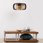 Lampa wisząca Crystal, 5-punktowa, w kolorze ciemnoszarym. Owalny klosz z przezroczystego tworzywa z centralnym źródłem światła, zawieszona na cienkich linkach. Ustawiona nad drewnianym stolikiem z metalowymi detalami.