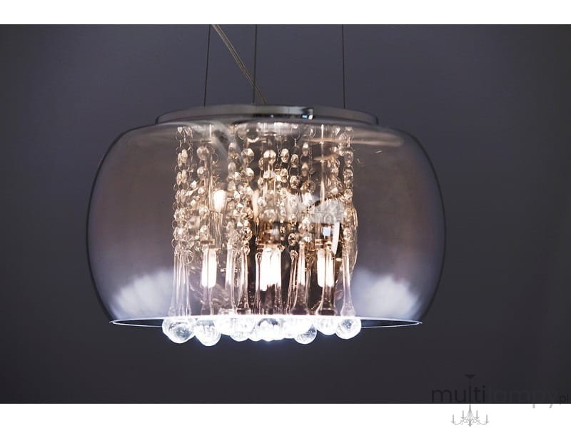 Lampa wisząca Burn 2, 6-punktowa, w chromowanej obudowie z przezroczystymi elementami. Kształt okrągły, z dekoracyjnymi kulkami i żarówkami wewnątrz. Zawieszona na cienkich linkach, w tle ciemna ściana.