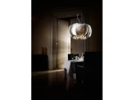 Lampa wisząca Burn 2, 6-punktowa, z chromowanym kloszem, zawieszona nad eleganckim stołem. W tle widoczne otwarte drzwi, ciemne wnętrze, stół nakryty białym obrusem z kieliszkami. Kształt klosza okrągły, przezroczysty, z dekoracyjnymi elementami.
