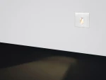 LED oprawa schodowa Lesel 001 L w kolorze srebrnym, zamontowana w ścianie. Posiada prostokątny kształt z wycięciem na źródło światła, emitującym delikatne światło na podłogę. Tło białe, podłoga ciemna.