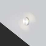 Oprawa schodowa Lesel LED 004 w kolorze srebrnym, okrągła, zamontowana na ścianie, emitująca ciepłe światło w dwóch kierunkach. Prosta, nowoczesna forma, idealna do oświetlenia schodów lub korytarzy. Tło w jasnym odcieniu szarości.