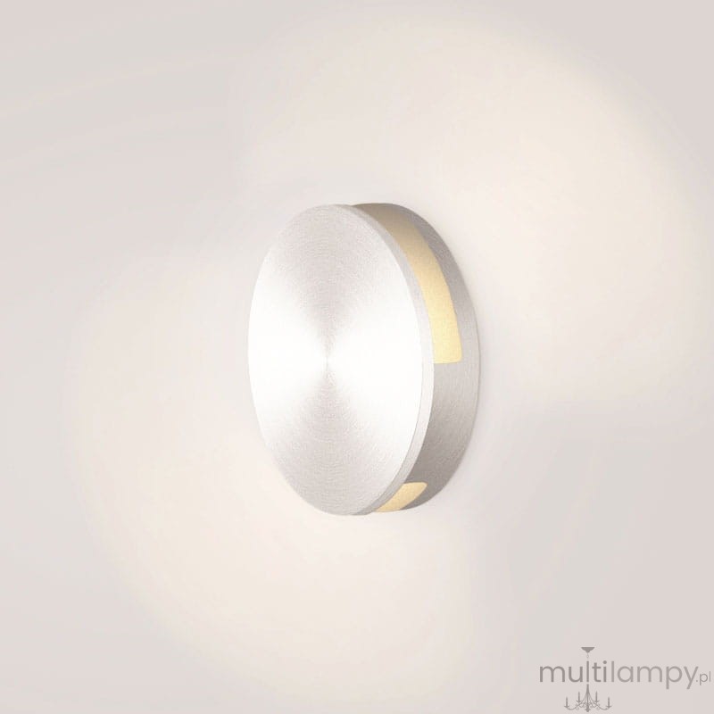 LED oprawa schodowa Lesel 004 w okrągłym, metalicznym wykończeniu. Montowana na ścianie, emituje ciepłe światło przez wąski pasek. Prosty, minimalistyczny design, idealna do oświetlenia korytarzy i schodów.