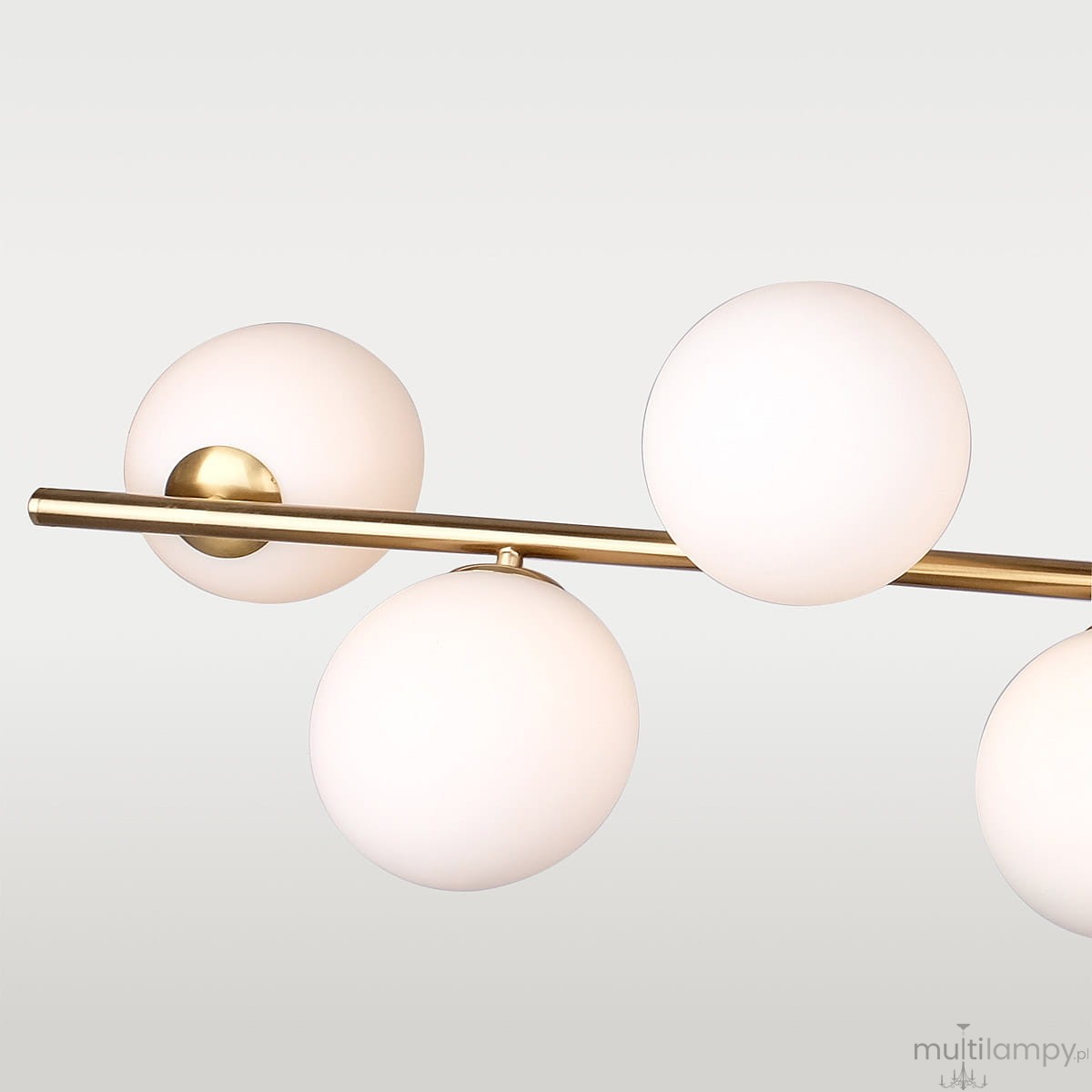 Lampa wisząca Cape Town 7-punktowa w kolorze mosiężnym z białymi, okrągłymi kloszami. Produkt zawieszony poziomo, z pięcioma kulistymi źródłami światła na metalowej rurze, na jasnym tle.