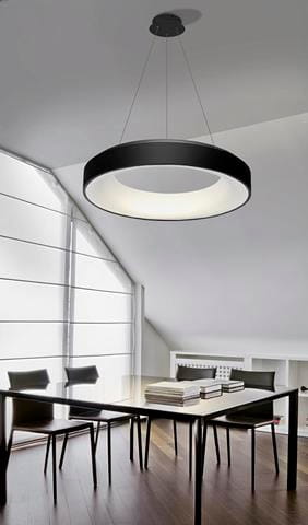 Czarna lampa wisząca Sovana D45 CCT LED z pilotem, o okrągłym kształcie, zawieszona nad stołem w nowoczesnym wnętrzu. Światło białe, emitowane z centralnej części, tworzy minimalistyczny efekt. W tle widoczne są proste, drewniane meble.