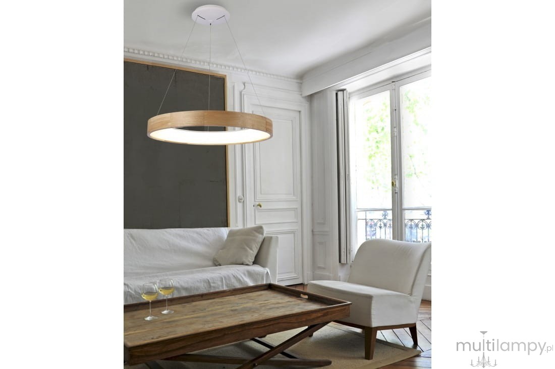 Lampa wisząca Silvam D45 LED w kształcie okręgu, z drewnianym obrzeżem i białym kloszem, zawieszona na cienkich linkach. Widok z góry, w jasnym pomieszczeniu z białymi ścianami i dużymi oknami. W tle sofa i drewniany stół z dwoma kieliszkami.