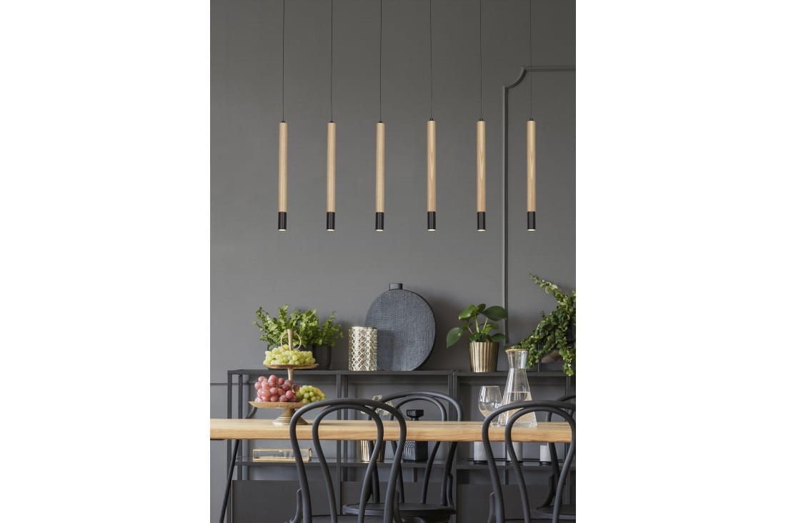 Lampa wisząca Izolda LED 6-punktowa w kolorze czarnym, z sześcioma prostokątnymi, drewnianymi kloszami u góry z czarnymi końcówkami. Zawieszona nad drewnianym stołem, w tle z zielonymi roślinami i dekoracjami na szarej ścianie.