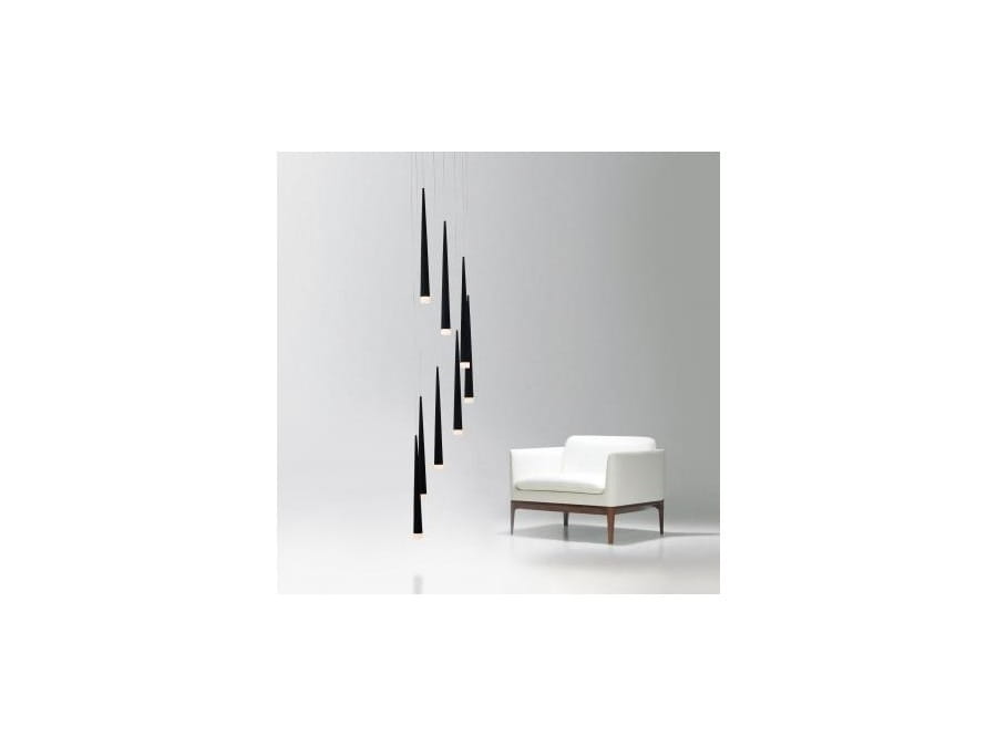 Lampa wisząca Stylo 8-punktowa w kolorze czarnym, z wiszącymi, stożkowymi kloszami. Ujęcie frontalne, z lampą zawieszoną nad białym fotelem. W tle proste, jasne tło, co podkreśla elegancję lampy.