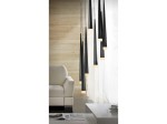 Lampa wisząca Stylo 8-punktowa w kolorze czarnym, o stożkowatym kształcie, z lampkami na końcach. Zawieszona nad białą sofą, w jasnym pomieszczeniu z drewnianą ścianą. Częściowo przezroczyste osłony lamp tworzą nowoczesny efekt świetlny.