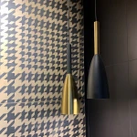 Czarna i złota lampa wisząca Solin LP-181/1P, w kształcie stożka, z metalowym wykończeniem. Zawieszona na cienkim kablu, prezentuje elegancki design. Tło w geometryczny wzór w odcieniach beżu i czerni, co podkreśla nowoczesny styl.