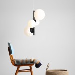 Lampa wisząca Bloom 4-punktowa w kolorze czarnym, z trzema białymi, okrągłymi kloszami o matowej powierzchni, zawieszona na cienkim przewodzie. W tle drewniane krzesło z kolorowym kocem oraz pleciony kosz.