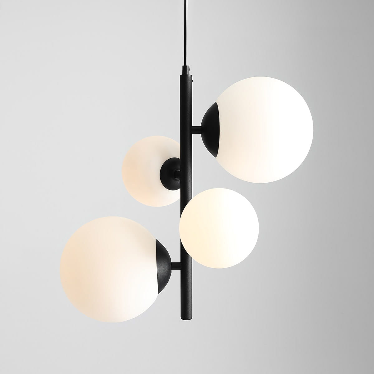 Czarna lampa wisząca Bloom z czterema okrągłymi kloszami w odcieniach bieli, umieszczona na centralnej czarnej podstawie. Klosze mają matową powierzchnię z częściowym wykończeniem w kolorze czarnym. Produkt zawieszony na cienkim przewodzie,.